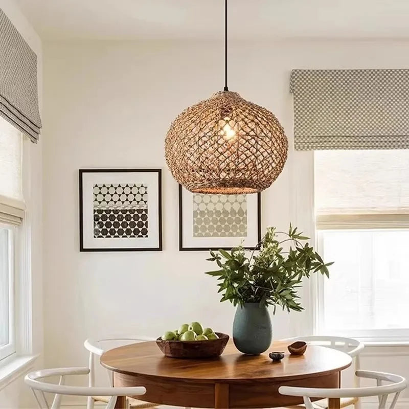 A single woven bamboo pendant light with a spherical shape hanging above a wooden dining table with chairs.