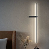A black minimalist LED strip wall sconce mounted on a textured wall, casting a warm glow.