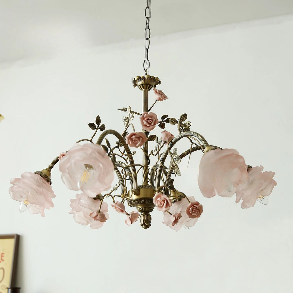 A brass chandelier with multiple pink rose bud and flower embellishments and frosted glass shades.
