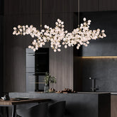 A wide shot of a modern kitchen with a large, gold-colored chandelier shaped like a bunch of grapes hanging over the island.