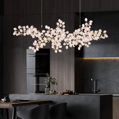 A wide shot of a modern kitchen with a large, gold-colored chandelier shaped like a bunch of grapes hanging over the island.
