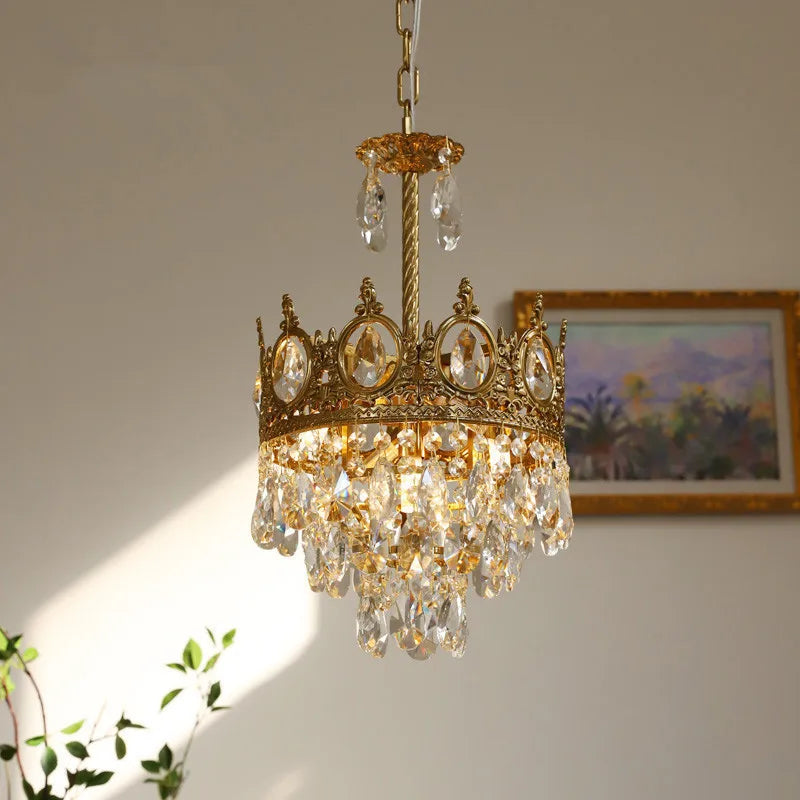 Gold chandelier with crystal accents hanging against a neutral wall with a painting in the background.