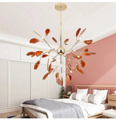 Gold leaf-shaped chandelier with orange accents hanging in a bedroom with pink walls and wooden furniture.