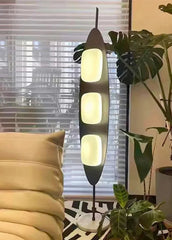 Modern floor lamp with three illuminated light bulbs in a living room setting.