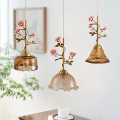 Three different styles of pendant lights, each with a brass stem adorned with pink rose buds and connected to variously shaped amber and clear glass shades.