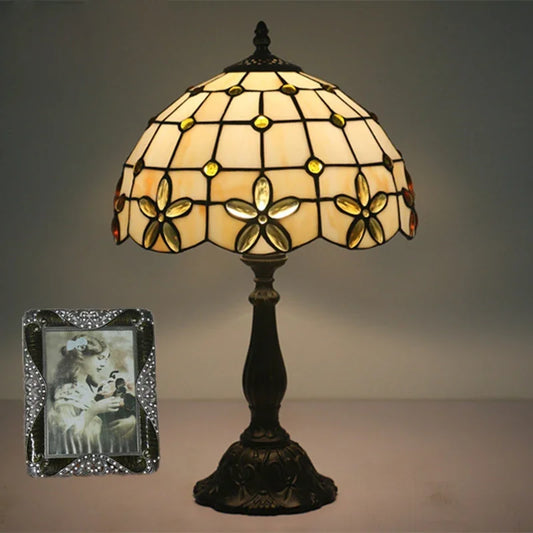 Tiffany stained glass floral table lamp with a dark base, shown with a framed photo.