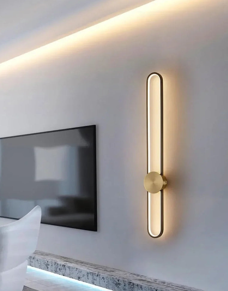 Modern wall-mounted light fixture on a neutral wall with a television in the background.