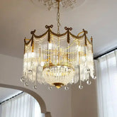 Gold tiered crystal chandelier with cascading glass rods and hanging clear crystal orbs, illuminated against a white ceiling.