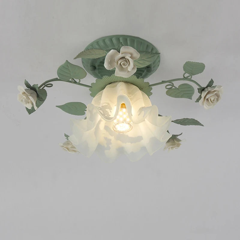 Close-up view of a green floral flush mount ceiling light with white roses and a ruffled glass shade with a visible E27 bulb socket.