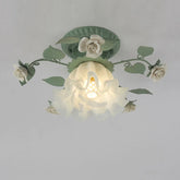 Close-up view of a green floral flush mount ceiling light with white roses and a ruffled glass shade with a visible E27 bulb socket.