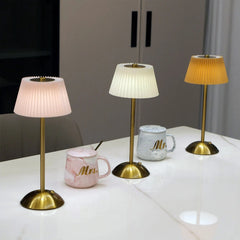 Three table lamps with pleated shades on a white surface, with mugs in the background.