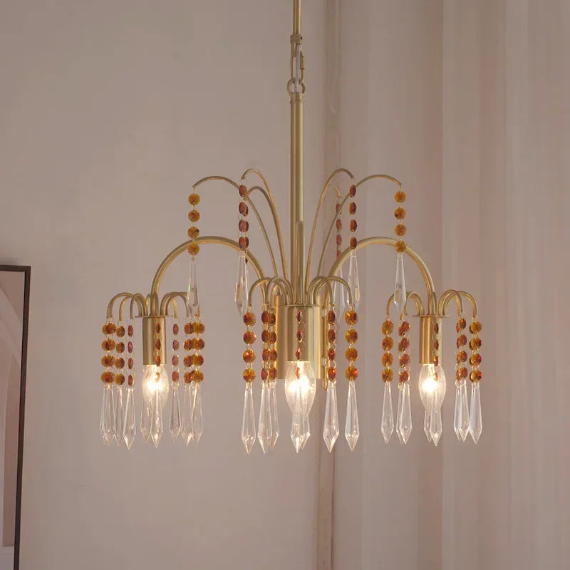 Close-up view of a gold chandelier featuring multiple arms adorned with clear crystal pendants and amber beads.