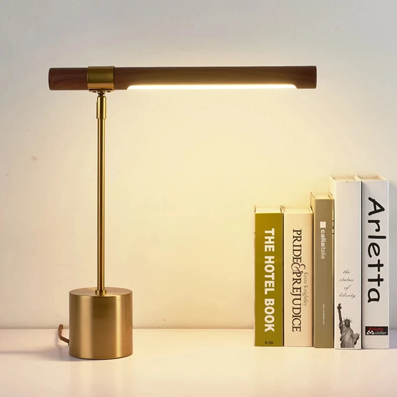 Brass and wood LED desk lamp with the light on, positioned next to a stack of books.