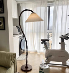 Modern living room with a floor lamp, exercise bike, and a window with sheer curtains.