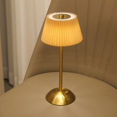 Gold table lamp with pleated beige shade on a beige surface