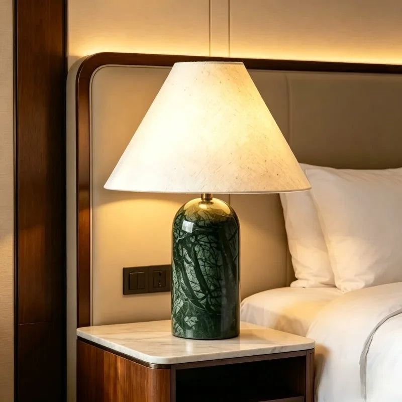 Green stone art ceramic table lamp with a fabric shade, placed on a nightstand next to a bed.