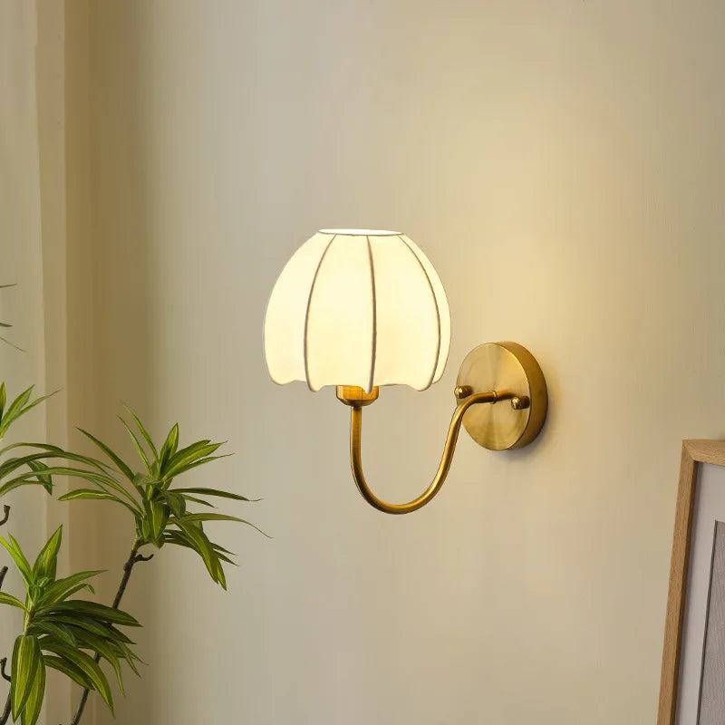 Wall-mounted lamp with a white shade and gold fixture on a neutral wall.
