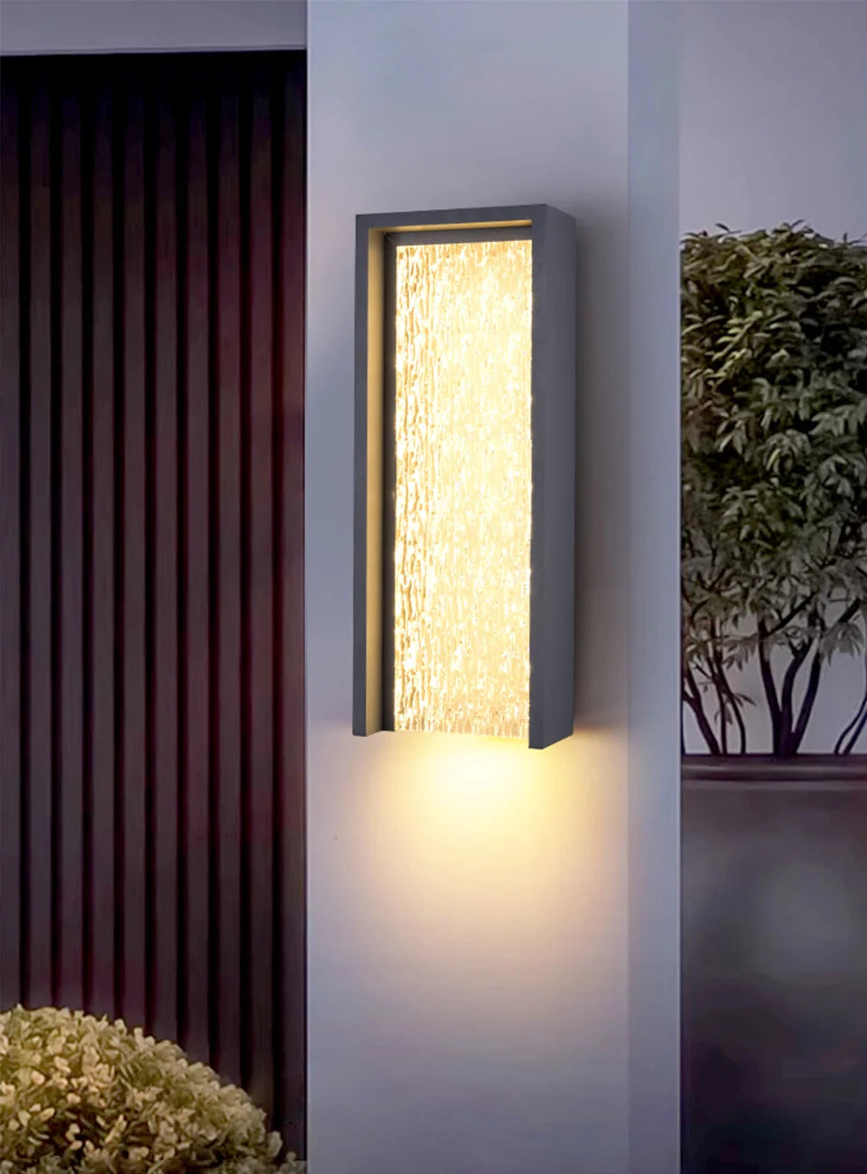 Modern outdoor wall light fixture on a building exterior with plants in the background