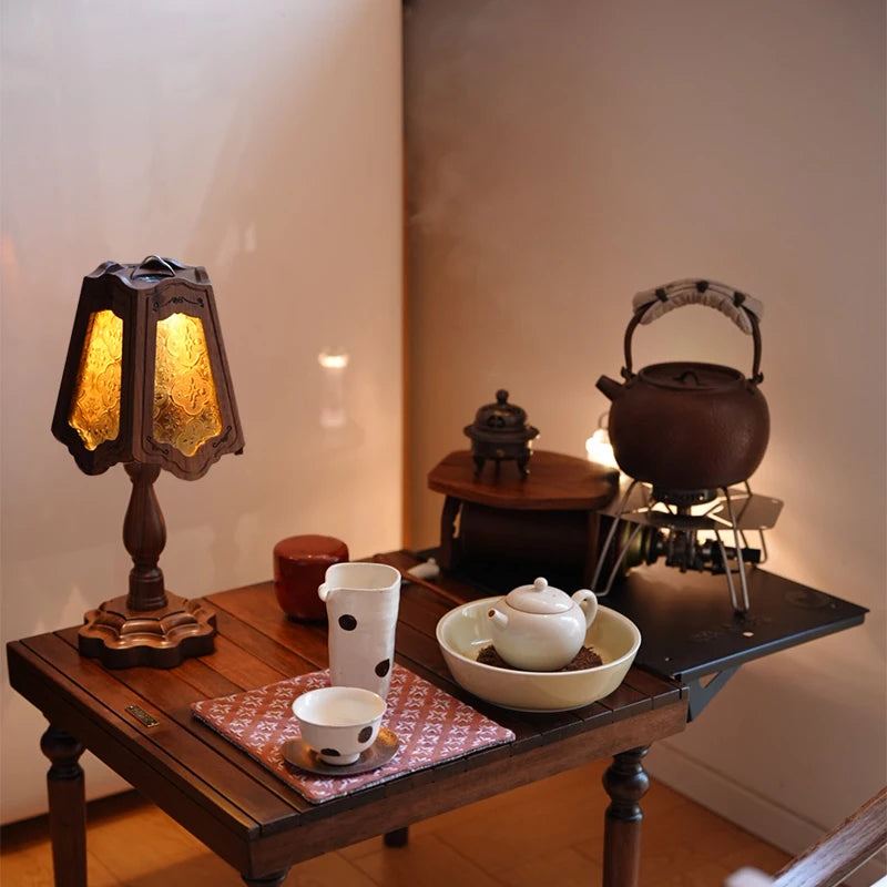 A table lamp with a black walnut and glass shade sits on a wooden table next to tea ceremony items.