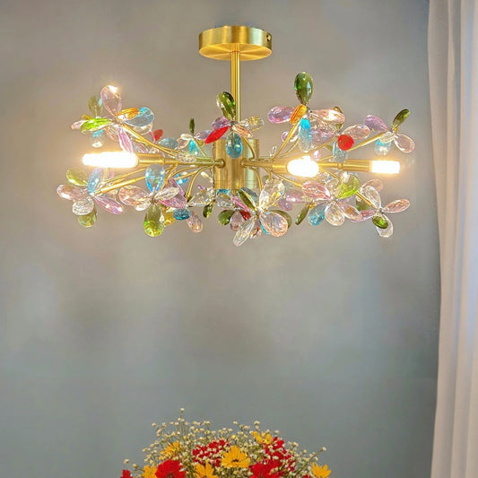 A gold-finished chandelier adorned with colorful crystal flowers and illuminated with integrated LED lights.