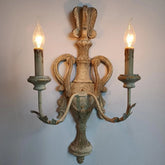 A distressed wood wall sconce with two candle-style lights against a light blue wall.