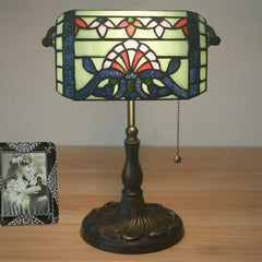 A stained glass table lamp with a green, red, and blue patterned shade and a bronze finish base, viewed from the front.