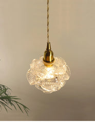 Side view of a brass pendant light featuring a detailed clear glass flower shade.