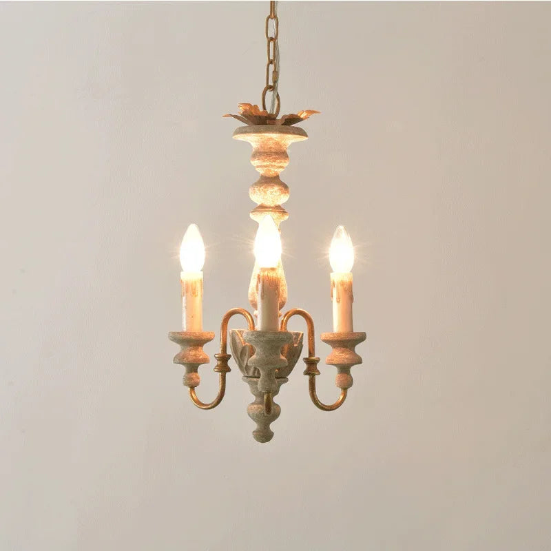 Close-up of a distressed wood candelabra pendant light with three exposed bulbs and golden accents, hanging against a white wall.