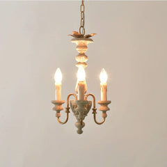 Close-up of a distressed wood candelabra pendant light with three exposed bulbs and golden accents, hanging against a white wall.