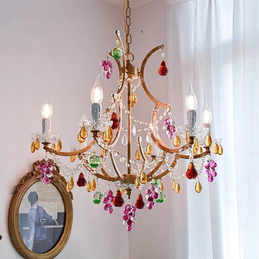 A gold chandelier with colorful crystal accents, resembling flowers and grapes, hangs from a ceiling.