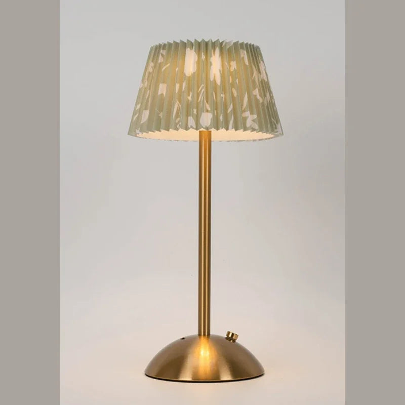 Table lamp with a gold base and pleated green shade on a light gray background