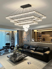Modern living room with a large chandelier, black sofa, and glass coffee table.