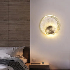 Modern wall sconce on a bedroom wall with a bed and nightstand in the background.