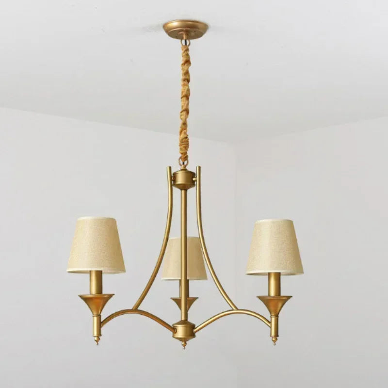 Gold chandelier with three beige lampshades on a light gray background