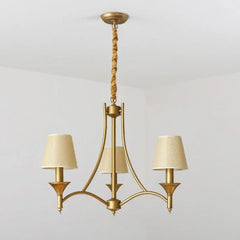 Gold chandelier with three beige lampshades on a light gray background
