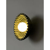 Black and gold fluted wall sconce with a warm LED bulb emitting light.
