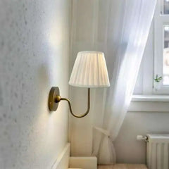 Wall-mounted lamp with white shade and brass arm in a room setting.