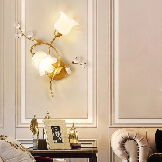 Gold floral leaf wall sconce with glass shades and crystal accents mounted on a beige wall.