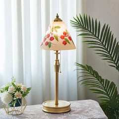 Decorative table lamp with floral design on a white surface with a plant in the background