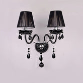 Black wall sconce with two fabric shades and cascading black crystals, mounted on a white wall.