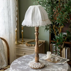 A wooden table lamp with a lace shade sits on a table next to a cup and saucer.