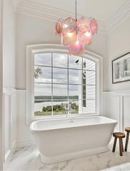 Bathroom with freestanding bathtub, pink chandelier, and large window view.