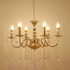 A gold chandelier with six candelabra-style arms, featuring clear teardrop crystals and candle-shaped LED bulbs, shown against a plain background.