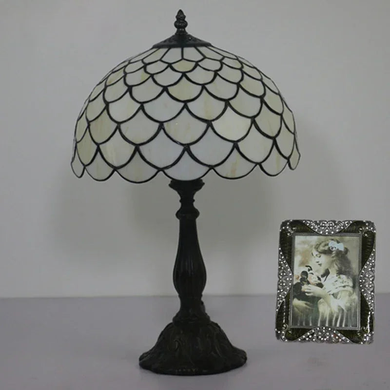 A Tiffany-style table lamp with a white and black stained glass dome shade and a dark iron base, shown on a side table next to a framed photo.