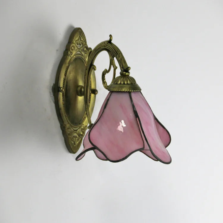 Wall-mounted light fixture with pink glass shade and gold metal fixture on a white background