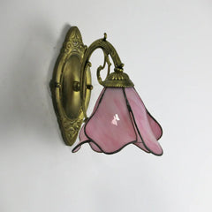 Wall-mounted light fixture with pink glass shade and gold metal fixture on a white background