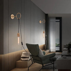 Two gold ring wall sconces illuminating a modern living room with a chair and fireplace.