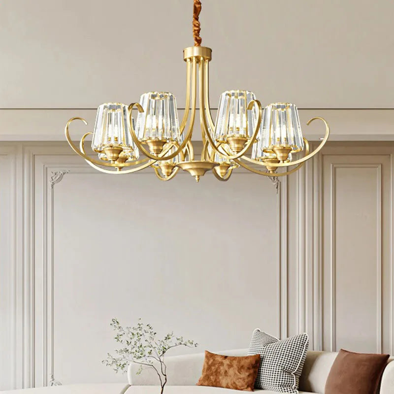 View of a polished gold chandelier with intricate floral details and crystal embellishments over a plush sofa.