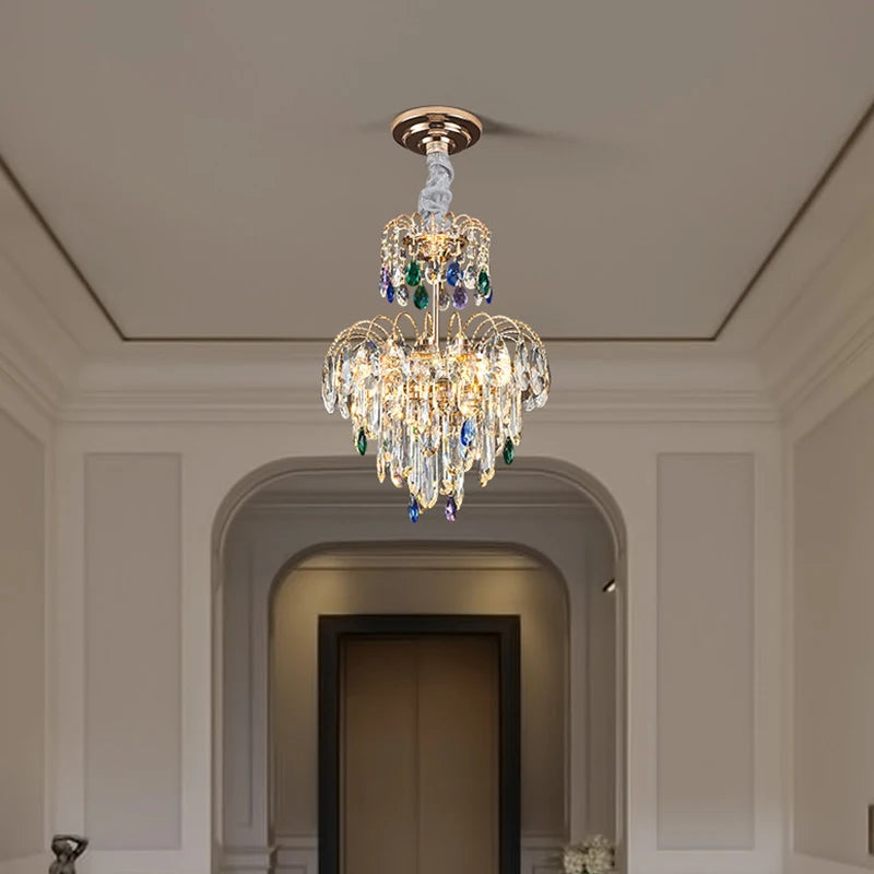 A gold multi-tier crystal chandelier in a well-lit hallway with an arched doorway in the background.