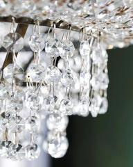 Close-up view of the faceted crystal droplets hanging from the polished chrome frame of a tiered crystal chandelier.